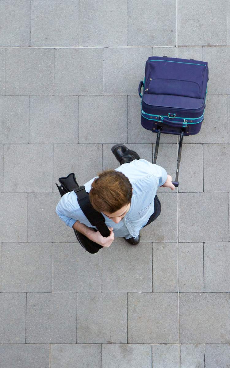 Reisender mit Trolley und Schultertasche am Flughafen.
