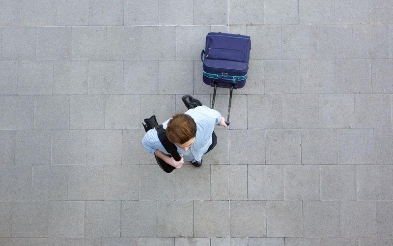 Reisender mit Trolley und Schultertasche am Flughafen.