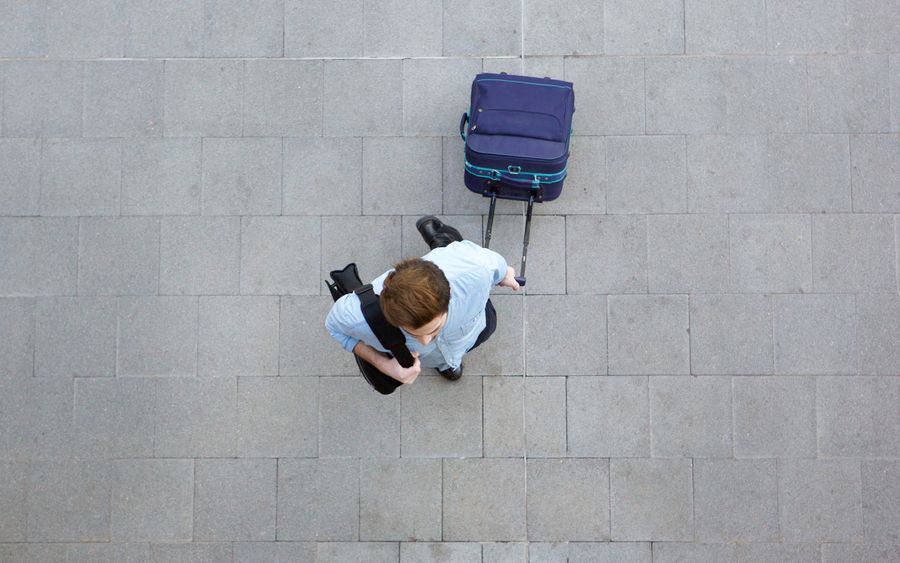 Reisender mit Trolley und Schultertasche am Flughafen.